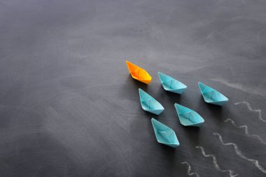 Karatahta arka planında kağıt tekne olan liderlik afişi konsepti. Bir lider gemi diğerlerine liderlik eder.