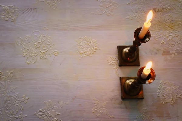 two shabbat candlesticks with burning candles over wooden table. top view. low key