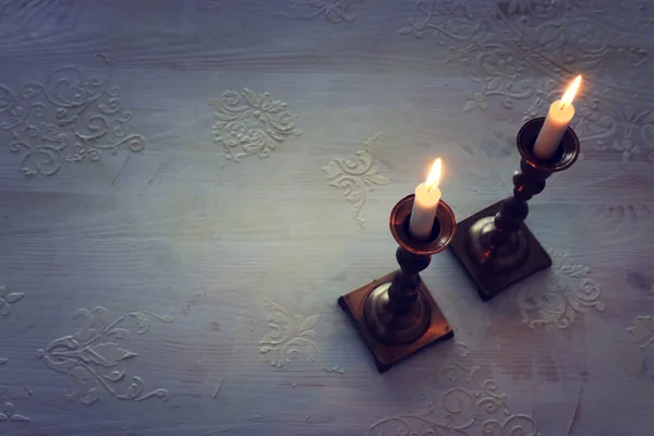 two shabbat candlesticks with burning candles over wooden table. top view. low key