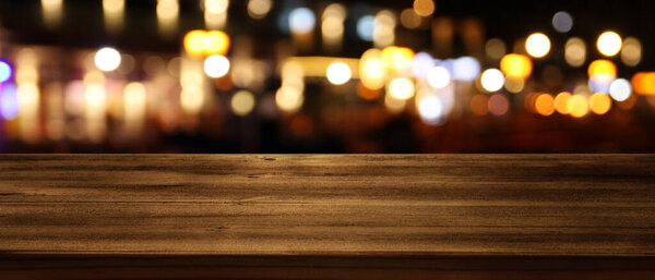 Изображение деревянного стола перед размытыми огнями ресторана