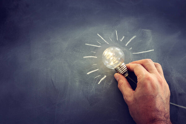 Education and business concept image. Creative idea and innovation. Man holding a light bulbs as metaphor over blackboard background