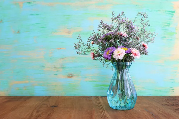 玻璃蓝色花瓶中木制桌子上方的五彩缤纷的野花花束 — 图库照片