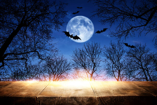 Halloween Holiday concept. Empty rustic table in front of scary and misty night sky, forest and full moon background. Ready for product display montage