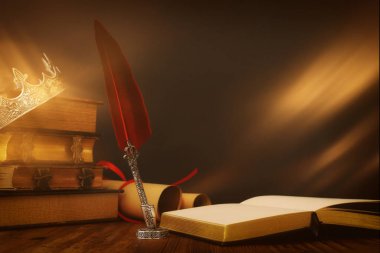 Güzel kraliçe / kral tacının eski kitabın üzerindeki görüntüsü ve ahşap masanın üzerindeki tüy kalem. fantezi ortaçağ dönemi