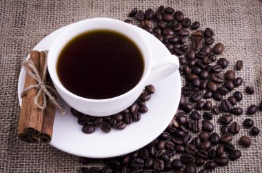 Tarçın ile beyaz bir fincan kahve bir çuval bezi arka plan üzerinde sopa