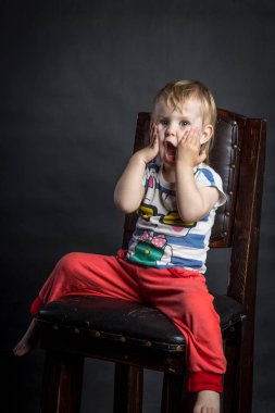 Bir çocuğun izole arka plan siyah stüdyo kahverengi ahşap sandalye üzerinde oturan kırmızı pantolon farklı duygular ile komik şirin portre