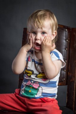 Bir çocuğun izole arka plan siyah stüdyo kahverengi ahşap sandalye üzerinde oturan kırmızı pantolon farklı duygular ile komik şirin portre