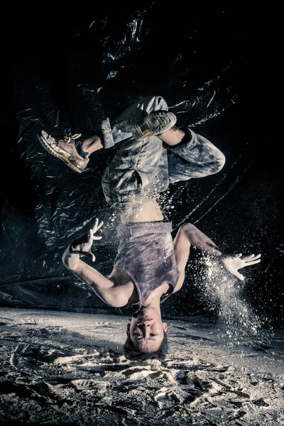cool dirty japanese  guy dancer in style of bboying doing complex tricks on floor in Studio filled with flour on black background. concept of space dance on surface of planet moon. toned sepia, instagram