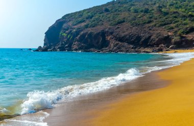 Güzel deniz sahilinde gündoğumu veya günbatımı günbatımı manzarası. Vahşi boş tropik sahil, mavi gökyüzü, sarı kumu, mountain view, bakınız dalga, manzara tarzı alınan güneş ışığı yansımaları kullanılabilir bir arka plan, duvar kağıdı, ekran koruyucu afiş seyahat vacat