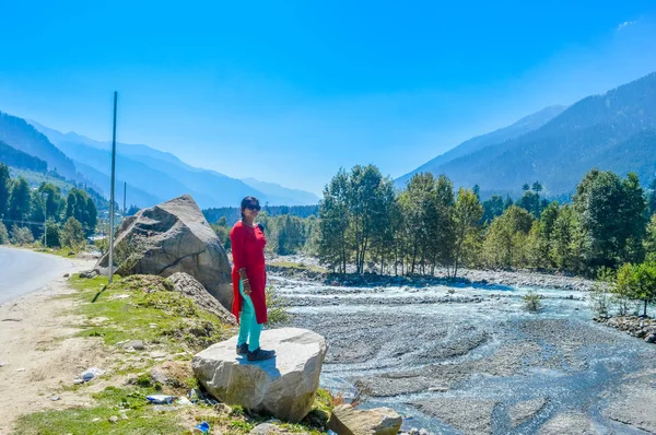 A lady in red drees standing on a bolder rock near a highway road. Beautiful landscape panorama view Himalayan valley of \