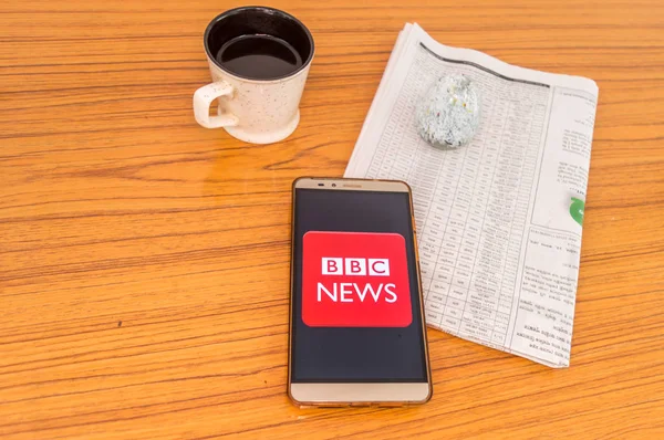 Kolkata (Inde), le 3 février 2019 : Une application de nouvelles de la BBC visible sur l'écran d'un téléphone portable superbement placée sur une table en bois avec un journal et une tasse de café. Un tir de produit technologique . — Photo