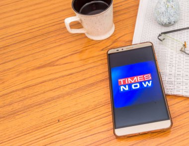 Kolkata, Hindistan, 3 Şubat 2019: Kez şimdi haber app (uygulama) güzel bir gazete ve kahve ile ahşap bir masa üzerine yerleştirilen cep telefonu ekranda görünür. Bir teknoloji ürün çekimi.