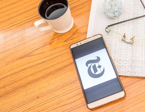 Kolkata, India, February 3, 2019: The New York Times news app visible on mobile phone screen beautifully placed over a wooden table with a newspaper and a cup of coffee. A Technology Product Shoot.