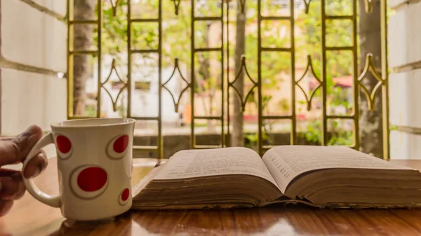Açık bir kitap, kahve fincanı, gözlük ya da gözlük, sıcak güneşli bir sabah, yakın çekim. Eğitim ya da Tatil Konsepti. Seçici odak içinde izole arkaplan, alanın sığ derinliği