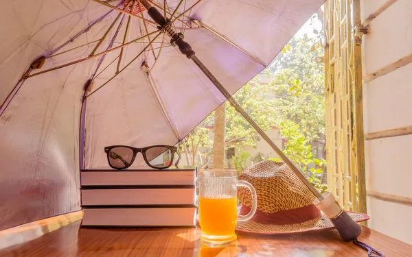 Sunburn risk concept protect skin from temperature. Umbrella protecting beautiful woman things. Books, sunglasses, orange juice and a straw hat. Summer holiday concept with copy space room for text.