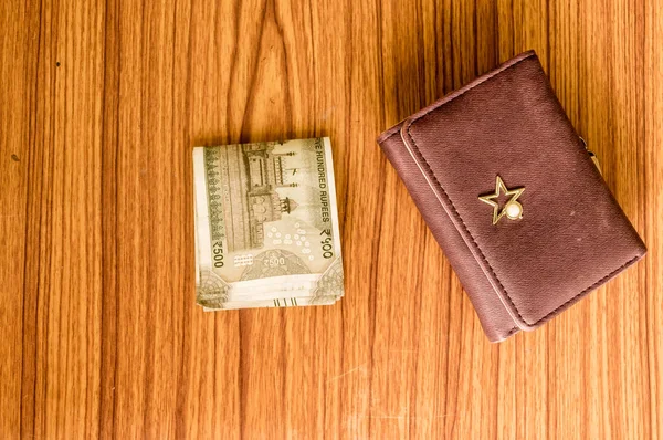 Ahşap bir masada kahverengi cüzdan deri çanta içinde Hint 500 rupisi nakit para. İş ekonomisi konsepti. Resmin sol tarafında metin için boşluk kopyalama odası olan yüksek melek görünümü.