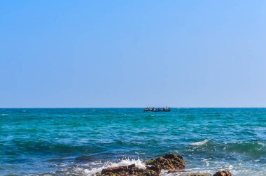 silhouette of people on small wooden rowing boat on the sea with blue sky and waves during sunset. Chilika lake Bay of bengal, State of Odisha, India. Travel holiday vacation concept. Copy space room.