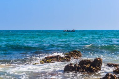 silhouette of people on small wooden rowing boat on the sea with blue sky and waves during sunset. Chilika lake Bay of bengal, State of Odisha, India. Travel holiday vacation concept. Copy space room.