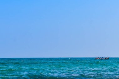 silhouette of people on small wooden rowing boat on the sea with blue sky and waves during sunset. Chilika lake Bay of bengal, State of Odisha, India. Travel holiday vacation concept. Copy space room.