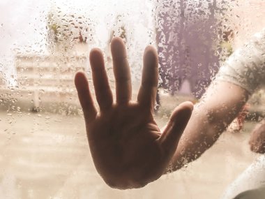 İnsan Eli, üzerinde Drops of Rain olan bir pencereye bastırdı. Su damlacıkları ile berrak bardağa dokunan el. Açık bulutlu ortamdan izole yağmur damlalarının Doğal Desen.