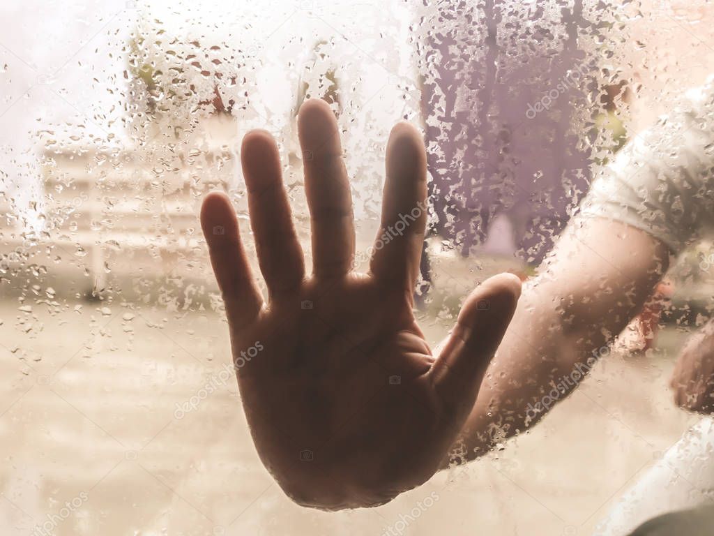 Human Hand pressed against a window with Drops Of Rain on it. Hand touching clear glass with water droplet. Natural Pattern of raindrops isolated from outdoor cloudy environment.