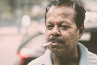 Portrait of a A mid adult senior mature man of Asian and Indian Ethnicity is smoking cigarette. Front View. Close up. Photography taken on 31 May 2019 on World No Tobacco or anti Tobacco Day, in a cit clipart