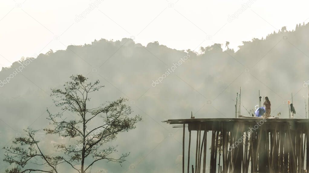 An unrecognizable young woman in the far distance standing on rooftop of an old under construction building surround with scenic shadow of majestic Himalayas mountain valley and pine woodland treetop.