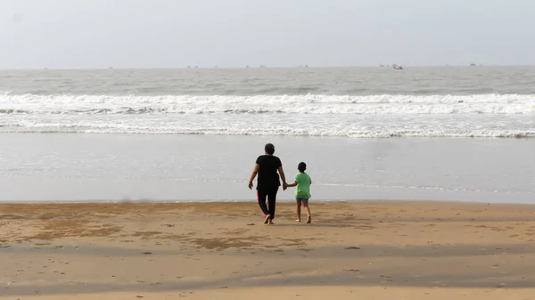 Rear View of Mother and son walking on a tropical beach in evening during sunset. The child admires his mom,s faith. Happy Mother���s day background concept. Goa, India, South Asia Pacific In Summer.