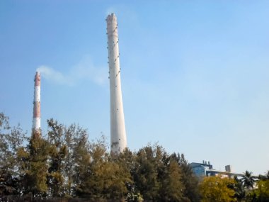 Factory chimney emits smoke, industrial smoke chimneys, Tall industrial factory chimney smokestacks ventilation to release smoke and steam Isolated against blue sky atmosphere background. Copy space clipart