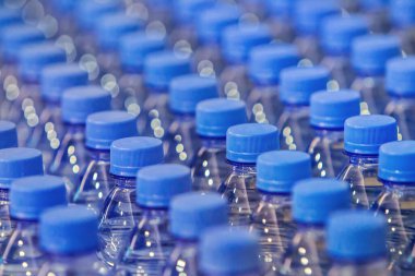 Sıralar dolusu plastik şişe. Plastik şişelerde temiz içme suyu bulunan plastik şişelerin boyunlarını kapatın, mavi şişe kapakları. Mavi arkaplan duvar kağıdı, yumuşak odak