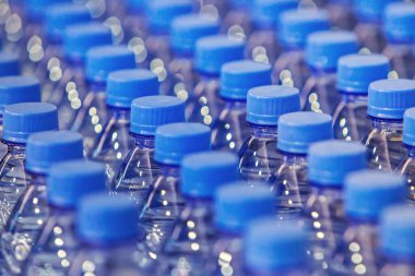 Geçmişi yok et, içkileri kapat. Plastik şişelerde temiz içme suyu bulunan plastik şişelerin boyunlarını kapatın, mavi şişe kapakları. Sıralar dolusu plastik şişe. Mavi arkaplan duvar kağıdı, yumuşak odak