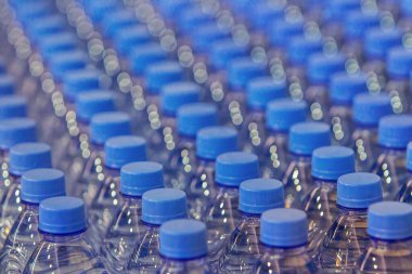 Plastik şişelerde temiz içme suyu bulunan plastik şişelerin boyunlarını kapatın, mavi şişe kapakları. Geçmişini sil, içkileri yakından çek. Mavi arkaplan duvar kağıdı, yumuşak odak