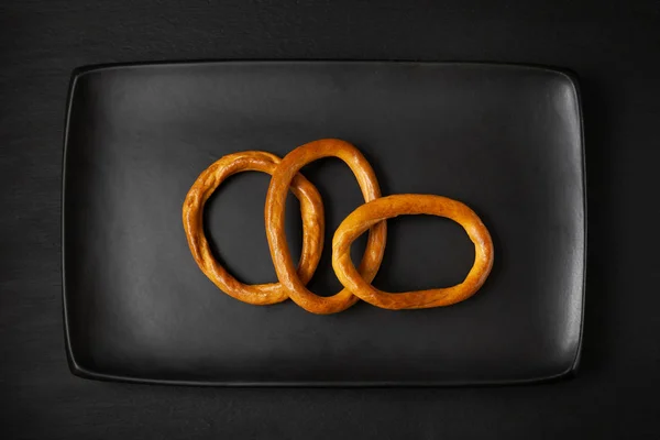 黒皿にベーグル。乾燥パンのリング、黒の背景にクラッカー. — ストック写真