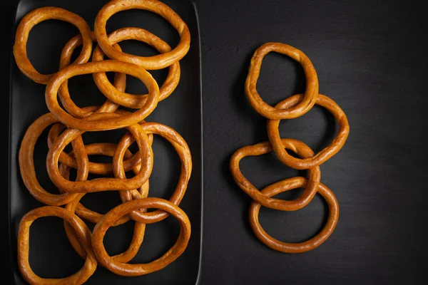 Simit siyah bir tabak üzerinde yığılmış. Kuru ekmek halkaları, siyah bir arka plan üzerinde siyah bir tabak içinde kraker. — Stok fotoğraf