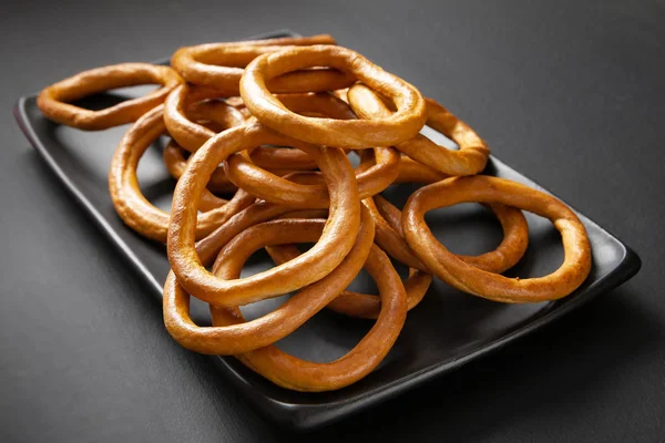 Muitos bagels empilhados em uma placa preta. Anéis de pão seco, biscoitos em uma chapa preta em um fundo preto . — Fotografia de Stock