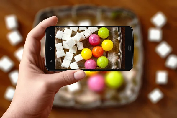 Мужские руки фотографируют еду на столе по телефону. Конфеты и сахар в серебряной тарелке на деревянном фоне. Фото смартфона для поста в социальных сетях . — стоковое фото