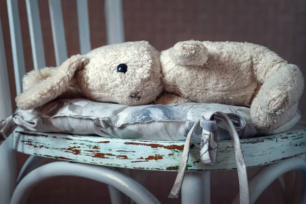 Vintage toy rabbit.Old vintage soft toy hare lying in vintage white chair.