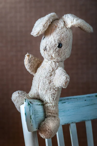 Vintage toy rabbit.Old vintage soft toy hare sits in old white chair.