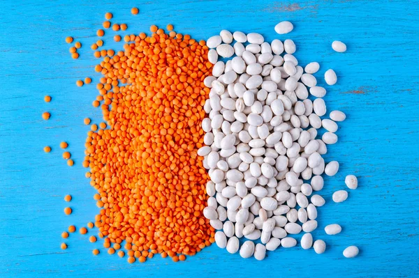 White beans and red lentils on a blue wooden background.