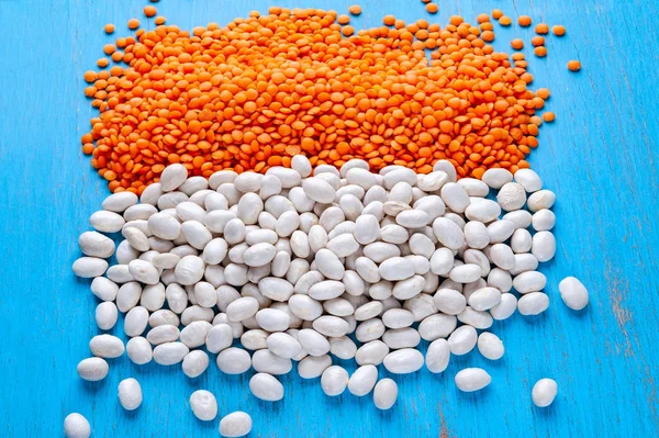 White beans and red lentils on a blue wooden background.