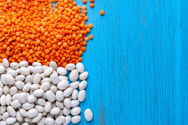 White beans and red lentils on a blue wooden background.