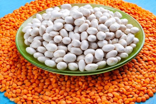White beans in a green plate and red lentils on a blue wooden background.