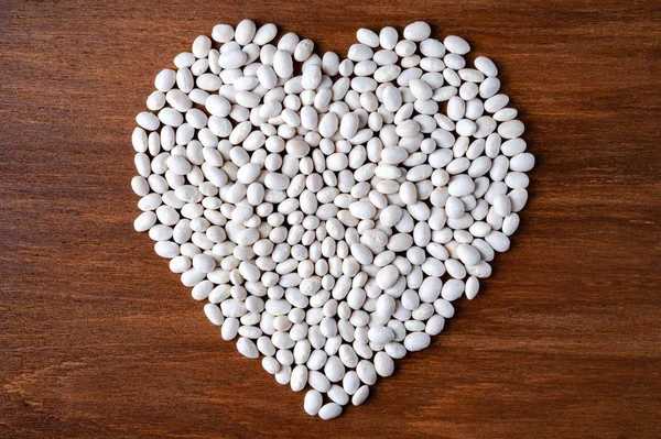 Mnoho bílých fazolí se Nalévalo do tvaru srdce na dřevěném pozadí. — Stock fotografie