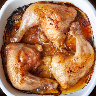 Bir fırın kabında kendi suyu yakın çekim içinde üst görünümü pişmiş tavuk bacakları.