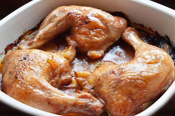 Baked chicken legs in their own juice close-up in a baking dish.