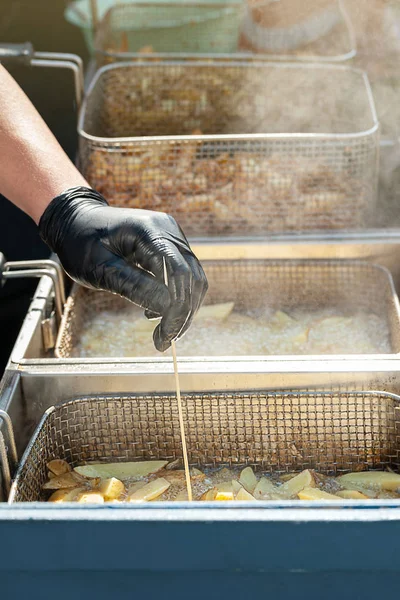 A mão do chef verifica a qualidade das batatas fritas. Batatas fritas fritas em óleo fervente em uma fritadeira . — Fotografia de Stock