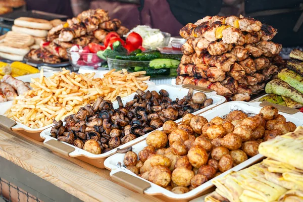 Street food. A lot of grilled meat, grilled mushrooms and grilled vegetables on the window of a street diner.