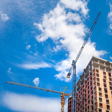 Beyaz bulutlu mavi gökyüzüne karşı vinçler ile şantiye.