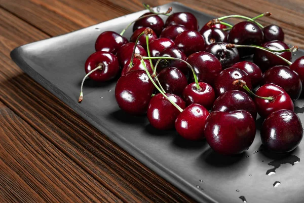 Frische reife, saftige Süßkirschen in einem schwarzen Teller auf einem hölzernen Hintergrund. nasse frische Kirschen mit Wassertropfen. — Stockfoto