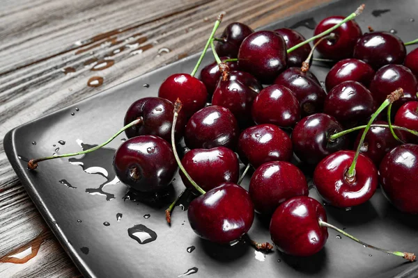 Ripe juicy sweet cherries in a black plate on a wooden background. Top view wet fresh cherries with water drops.